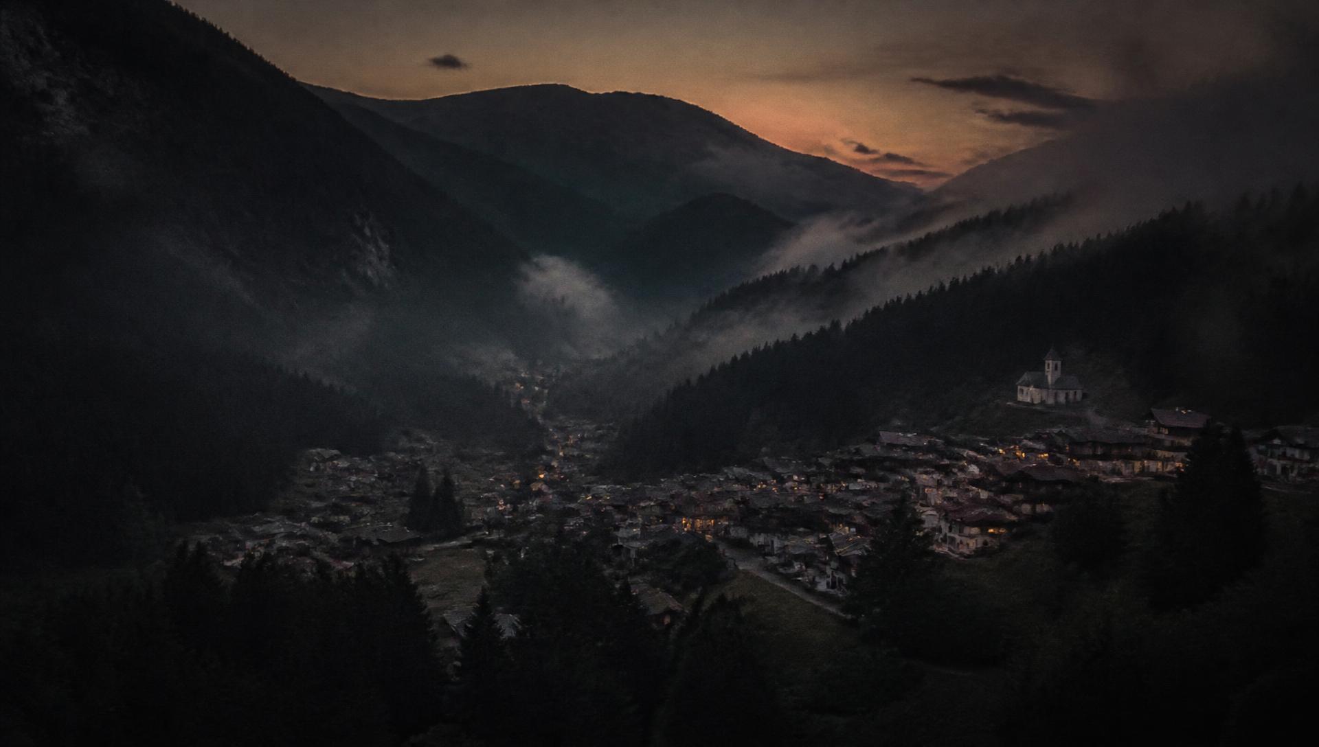Alpine town in a misty valley at dusk, seen from above